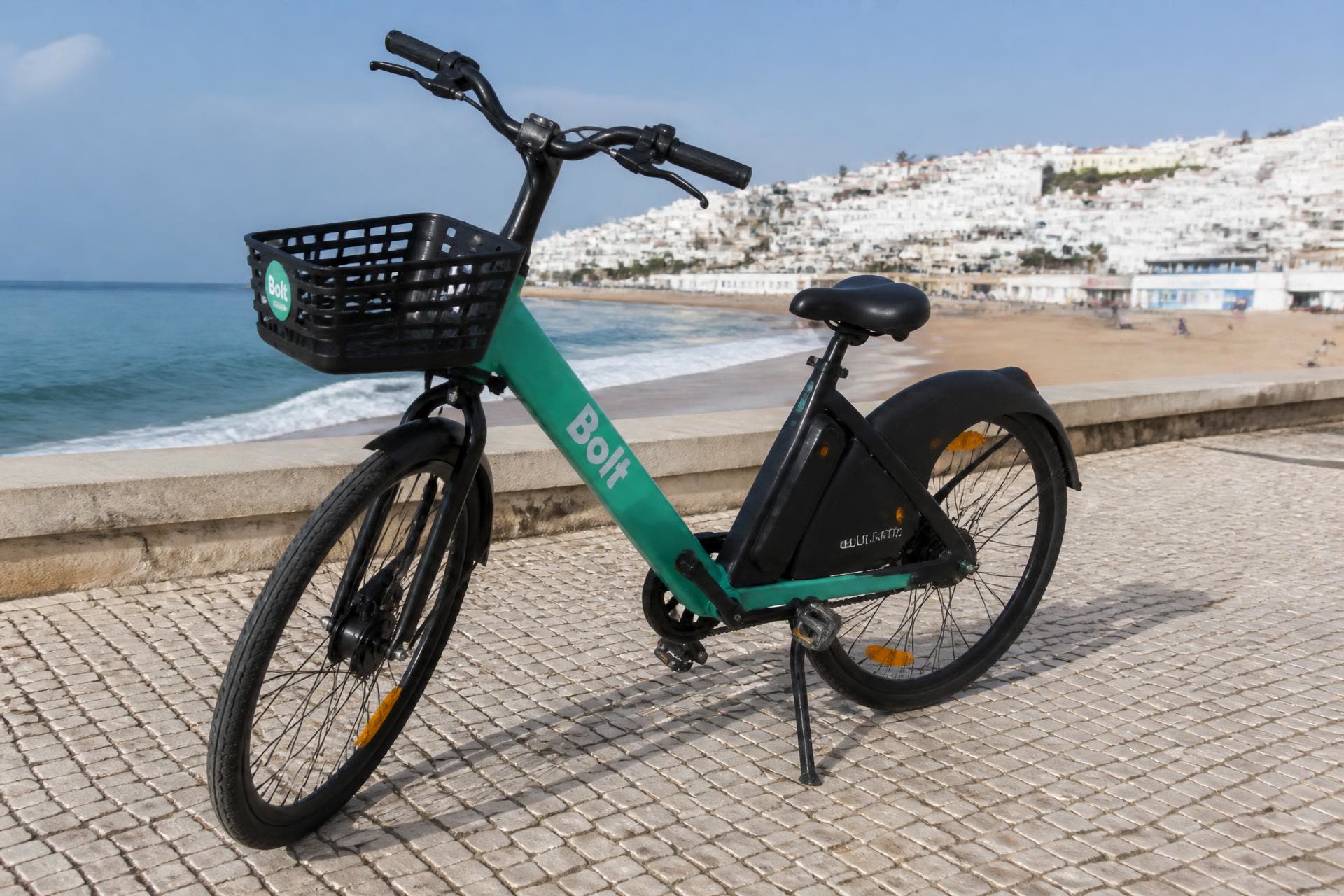A rental electric bike parked on the cobbled seafront promenade beside Nazaré beach