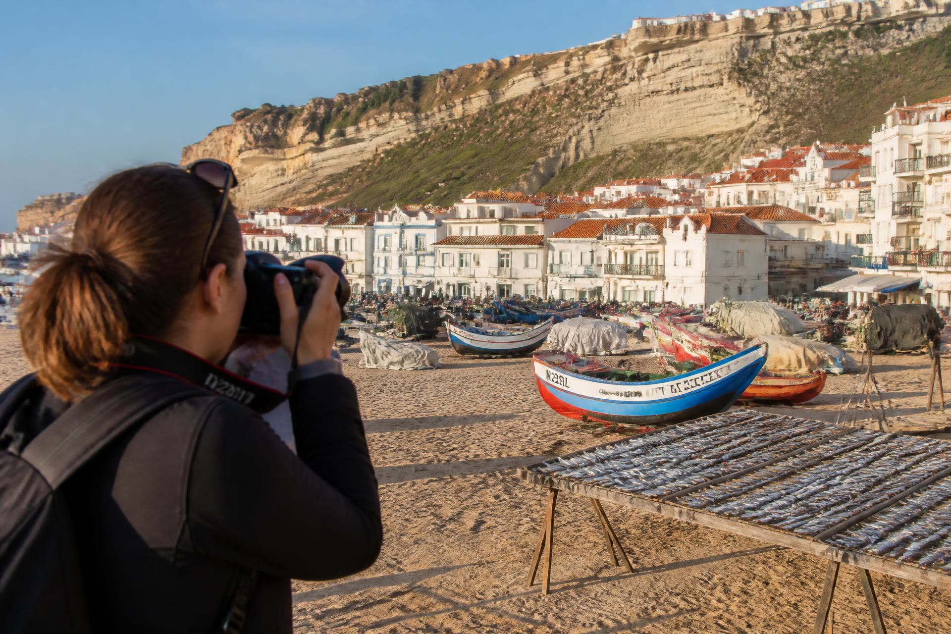 A photographer shooting the painted fishing boats and fish-drying racks on Nazaré beach
