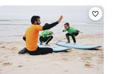 Instrutor e aluno em fatos de surf a levar pranchas para o mar